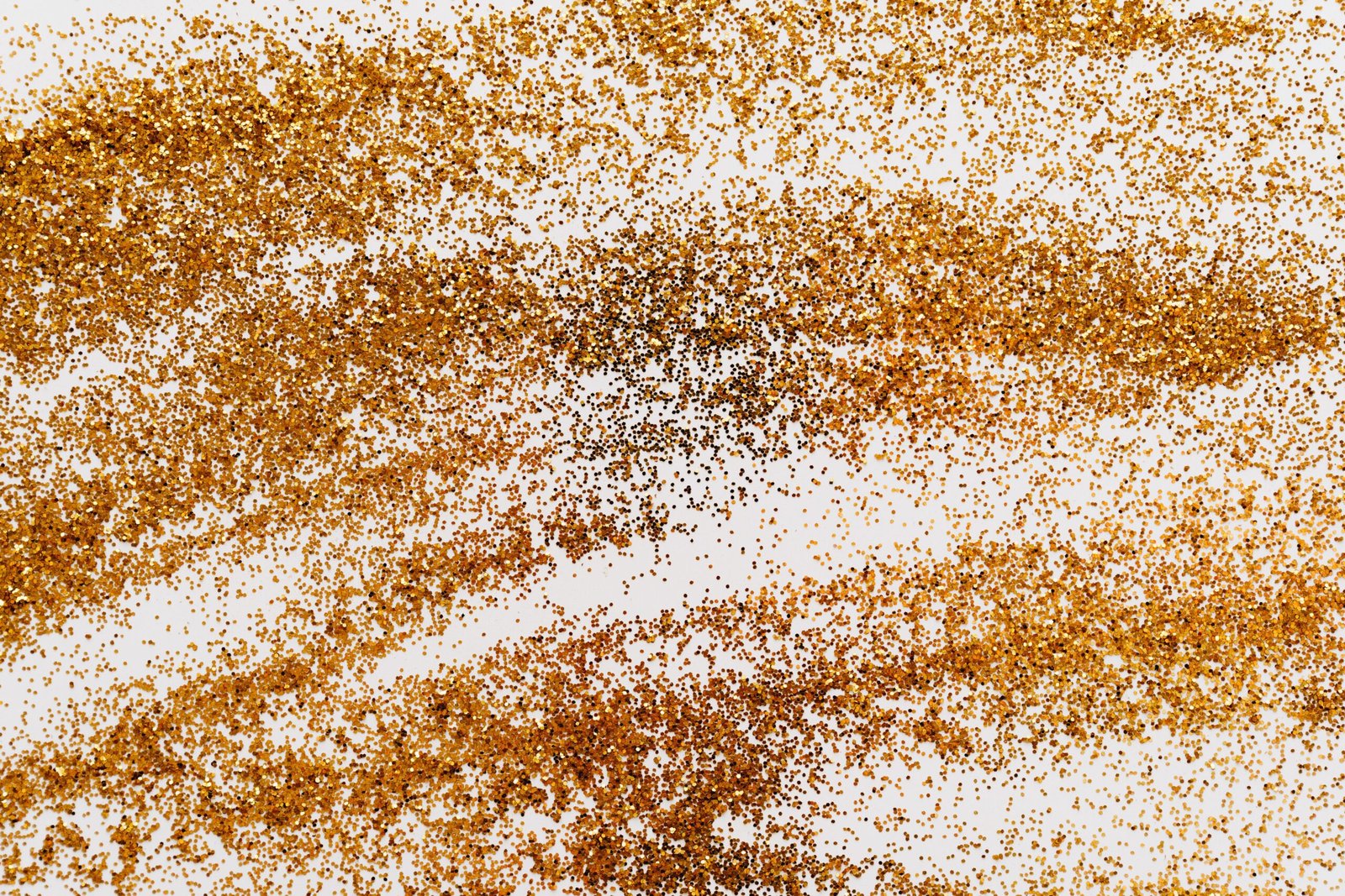 A shimmering abstract pattern of gold glitter scattered on a white surface for decoration and design.